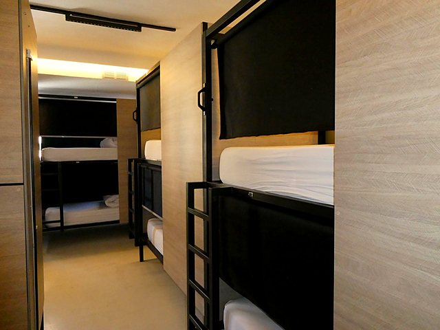 Shared hostel room with wooden bunk beds, each with its own curtain