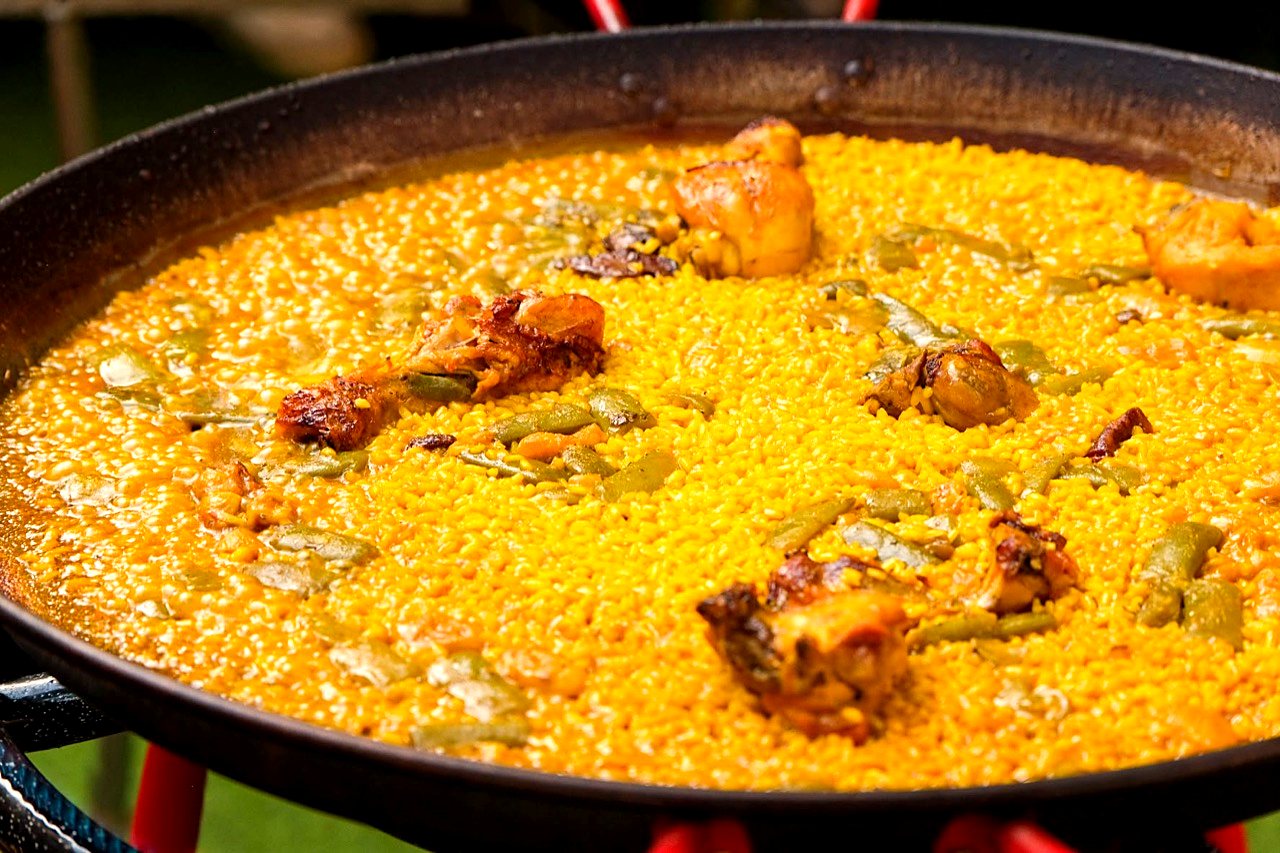 Close-up of paella valenciana with chicken and flat green beans, the rice still bubbling in the pan