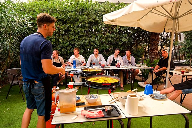 The cook talking a table of guests through each step during a paella workshop in a Valencia garden
