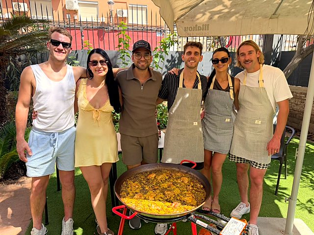 Group in striped aprons posing behind the paella they cooked